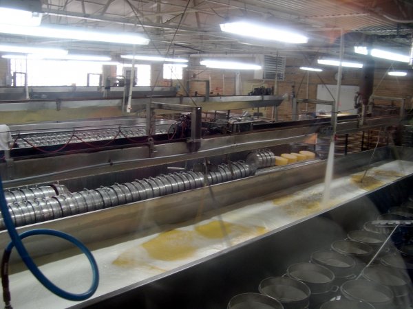 Foreground: Vats full of curds and whey; Background: Cheese presses (each tin is a wheel of cheese)